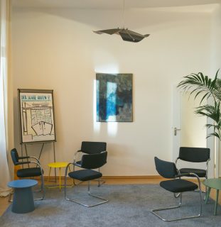 Heller Beratungsraum mit Stuhlkreis, Flipchart und einem Gemälde an der Wand