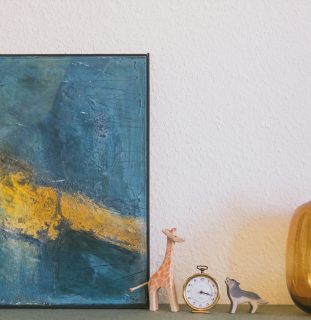 Gemälde an der Wand, davor kleine Figuren und eine Taschenuhr